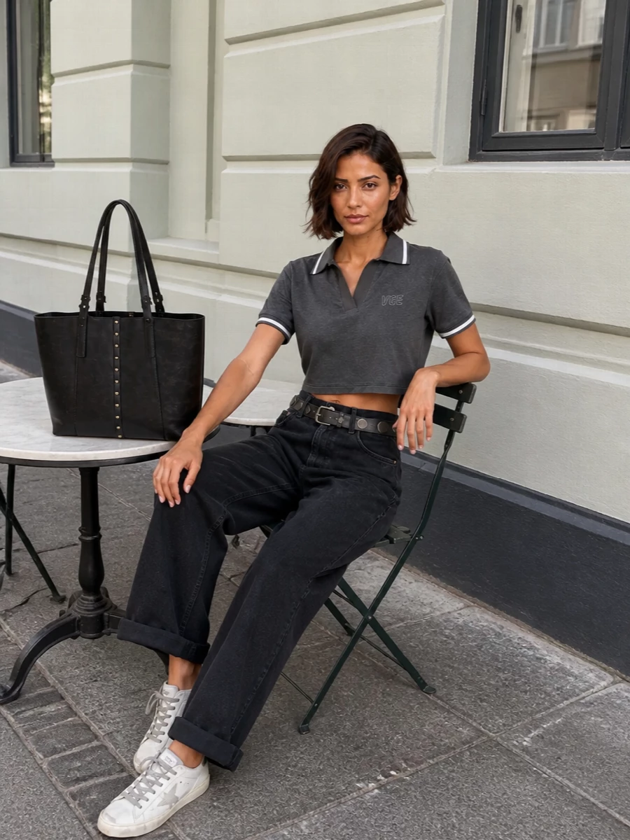 Charcoal varsity polish meets downtown denim in a cropped polo paired with high-rise washed-black wide-legs for an easy, athletic take on streetwear. Monochrome sneakers keep the palette tight around grey, black and off-white, while a washed-black tote and studded belt sharpen the attitude just enough for city days that run long.