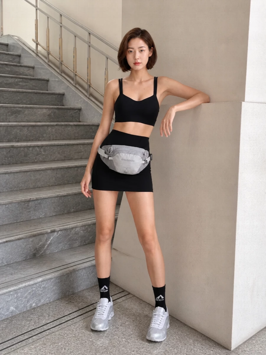 A tight black Nike set keeps everything clean and close to the body, with the high-rise mini short meeting the cropped tank for a sharp, uninterrupted line. White and silver runners break the monochrome just enough, while a low-slung technical belt bag and graphic socks make it feel considered for both studio and city.