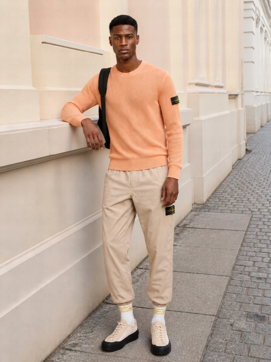 Soft apricot up top and light beige down low keep this Stone Island set clean, sporty and sun ready. Neutral technical sneakers and a black backpack ground the colour with a clear street edge. It is an easy airport-to-city uniform that still feels considered through texture, taper and quietly graphic details.