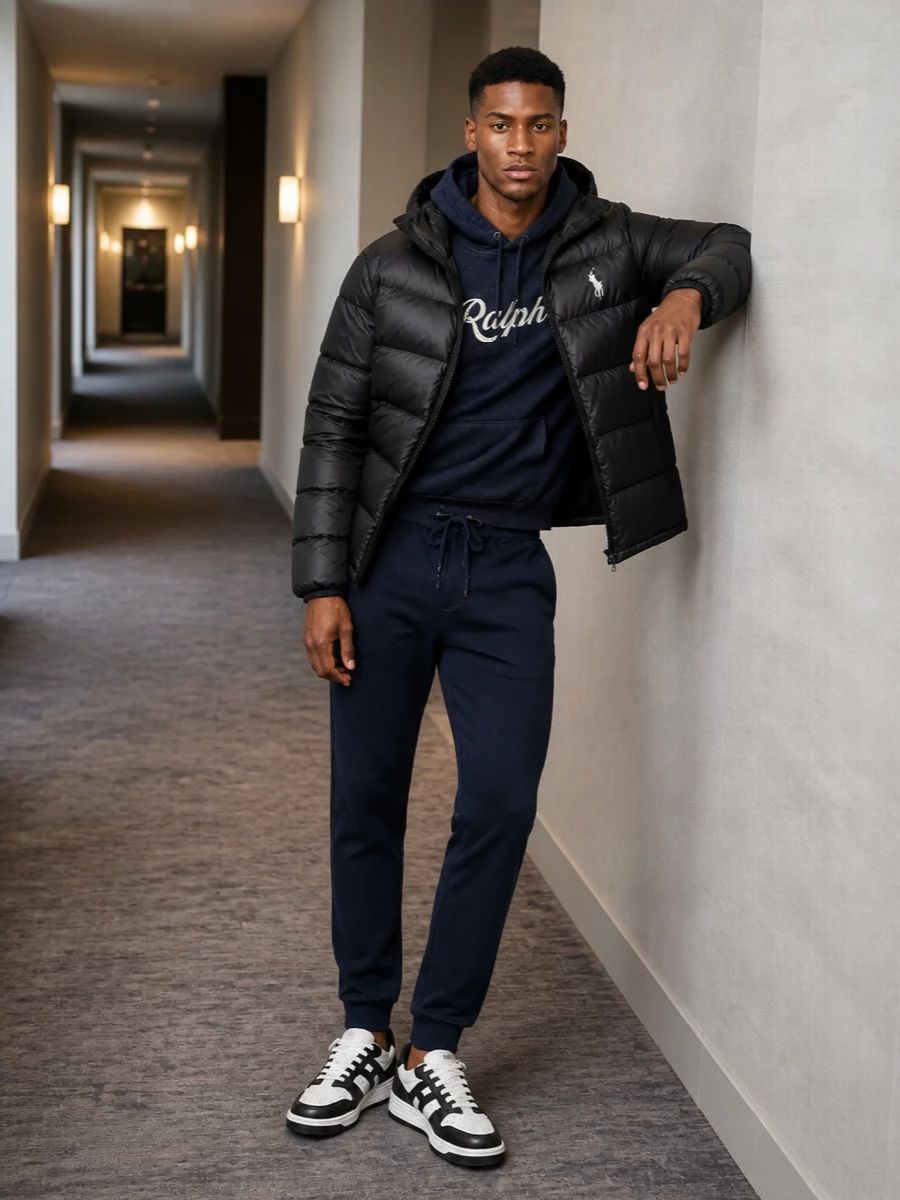 A black Polo puffer sits over washed navy layers and tailored joggers for a tight, collegiate street take on cold city days. Black and navy stay in quiet dialogue, with monochrome Hogan courts and a padded Moncler tote keeping the mood technical and polished without feeling overthought.