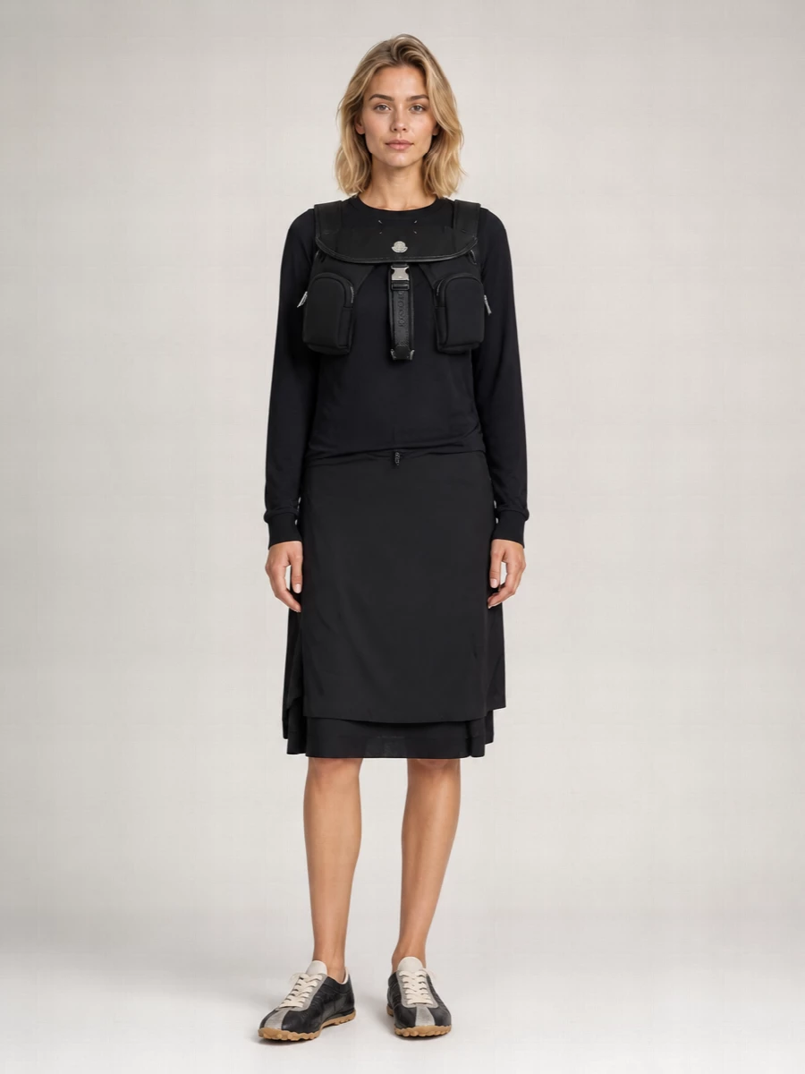 Anchoring the outfit with the dress route keeps the story clean and directional, pairing the Moncler backpack with a single, fluid Margiela column and intelligent, low-key details. The layered black dress and textural sneakers sit firmly in a quiet-luxury, art-school street mood that works for city days moving between galleries, cafés and meetings. Everything stays within a monochrome, softly tonal palette so the silhouette and materials do the talking rather than overt logos.