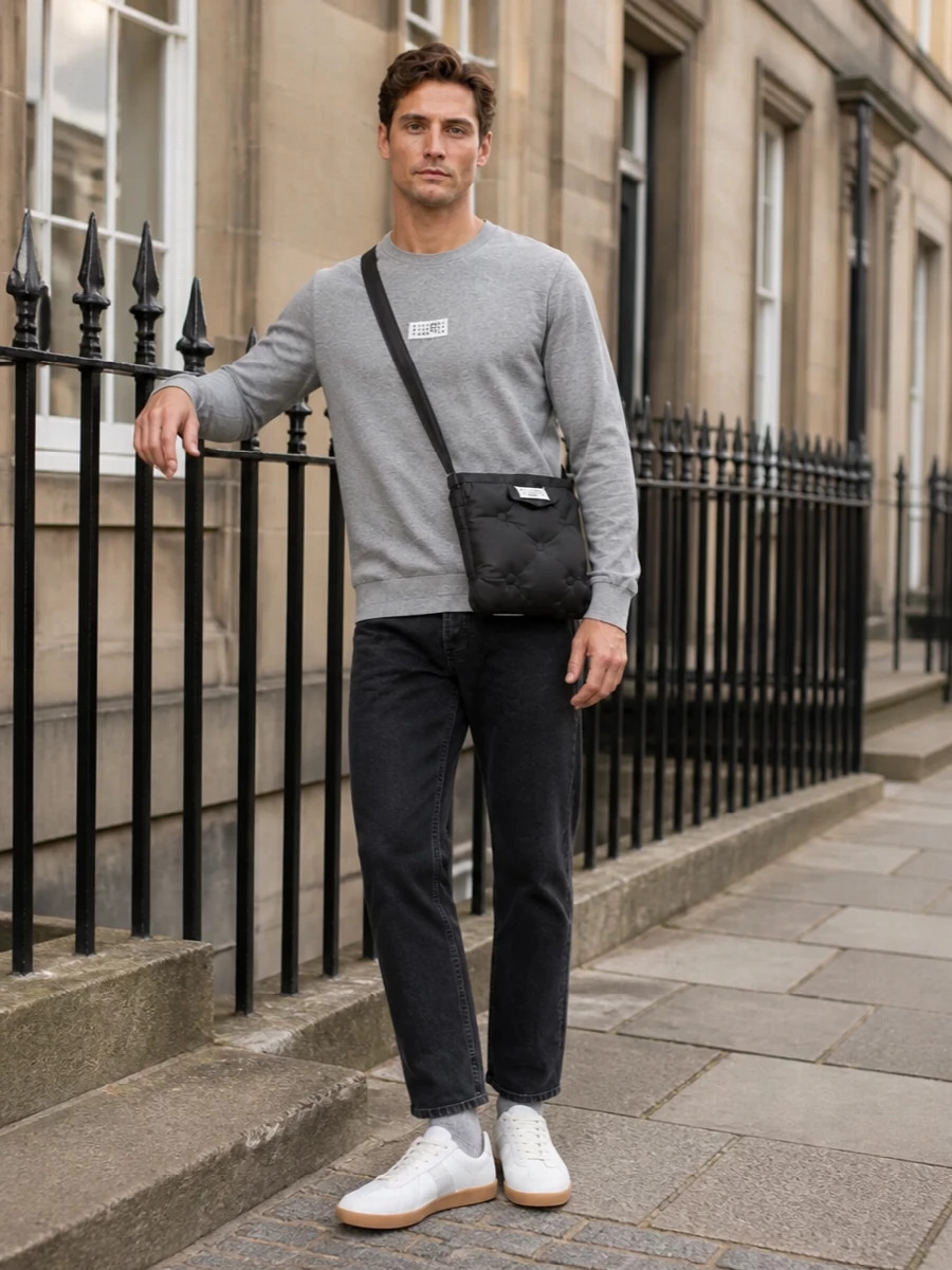 Heather grey jersey and washed-black denim set up a low-contrast, quietly precise base that feels relaxed but intentional. Off-white gum-sole sneakers and the padded crossbody keep the mood soft and Margiela-centric rather than logo-heavy. Grey socks finish the story with a barely-there link between top and ground, so the whole outfit reads as one continuous, muted line.