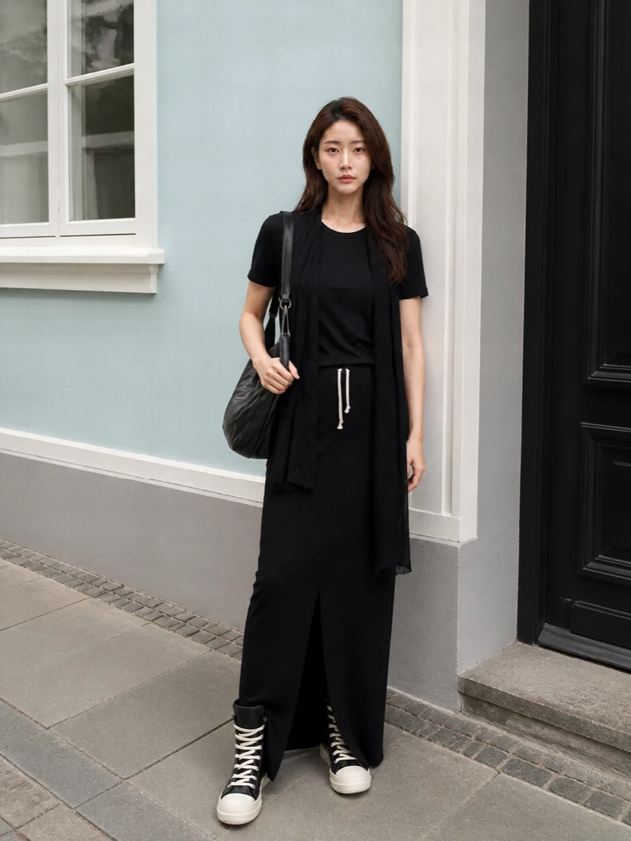 A long black Rick Owens column, from tee to drawstring maxi skirt, reads clean and decisive yet relaxed. Signature high-top sneakers and a crumpled crescent bag keep it grounded in streetwear, while the raw scarf texture adds subtle depth for colder days. The result is a stealth monochrome uniform that moves easily from studio mornings to late city evenings without changing gears.