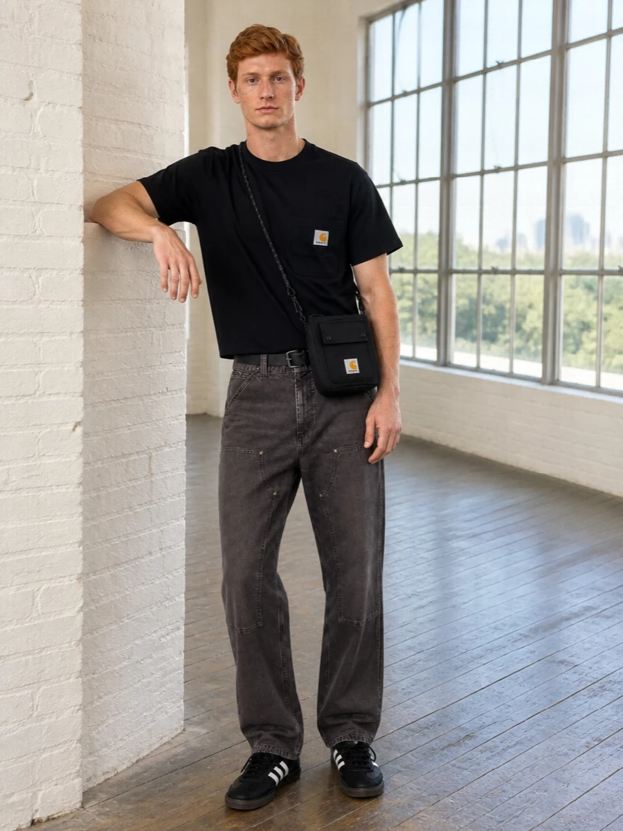 A black Carhartt pocket tee sits over relaxed charcoal workwear denim for a uniform-style base that feels easy but considered. Black gum-sole Adidas sneakers keep the line clean and low, while a compact Carhartt crossbody and a subtle Y-3 webbing belt add quiet function without breaking the monochrome mood. The result is a grounded city uniform with streetwear attitude and practical utility details front and center.