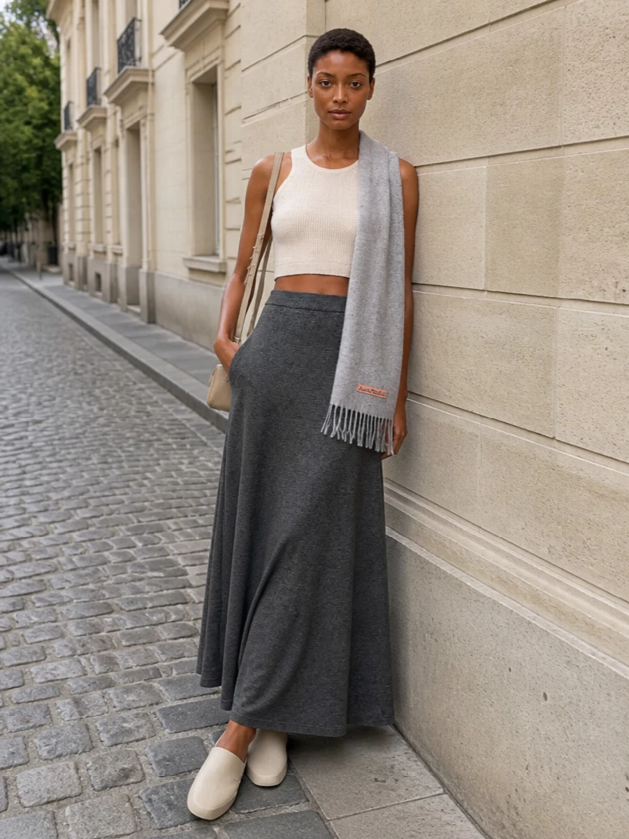 A cropped oatmeal knit meets a high-waisted charcoal maxi for a column that feels relaxed yet precise. Sculpted stone mules and a compact beige crossbody keep the palette soft and neutral, while a heather-grey scarf adds just enough texture to make the whole ensemble feel considered for cooler days.