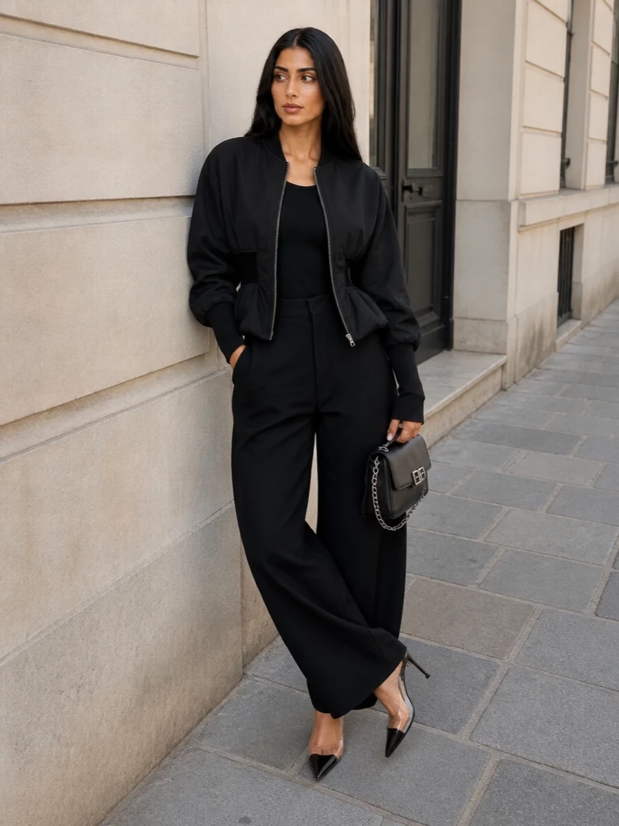 This look builds a fully architectural black column around Alaïa’s cinched bomber, using the ribbed bodysuit as a disappearing base and the sculptural high-waisted wide-leg trouser to amplify the hourglass line. Clear-strapped pointed mules and a silver‑chained Balenciaga shoulder bag bring in just enough hardware and transparency to echo the jacket’s zip, delivering a coherent, SS‑appropriate, gallery-to-night cocktail uniform. I chose the top-and-bottom route over a dress so the bomber remains the hero, with the proportions and volume intentionally engineered around its peplum waist.