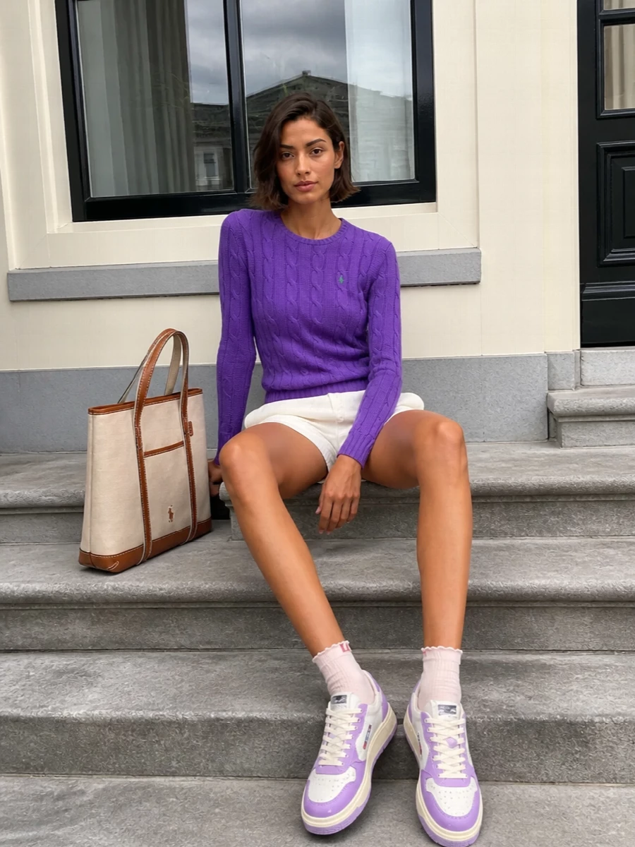 Violet cable knit meets airy off white shorts for a crisp, preppy take on off duty dressing. Lavender-accented sneakers and a structured canvas tote keep it polished for city errands and coffee runs. Frilled ankle socks add a small, playful twist without disrupting the clean, sporty lines.