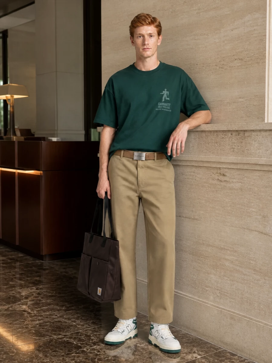 Forest green and khaki sit together in a relaxed, clean workwear mix that feels easy but intentional. The straight, roomy trouser keeps the tee’s boxy shape balanced, while the retro green-accented high-tops pull the color story down to the ground. A dark utility tote and sand-toned belt finish it with practical texture that still feels street ready, not precious.