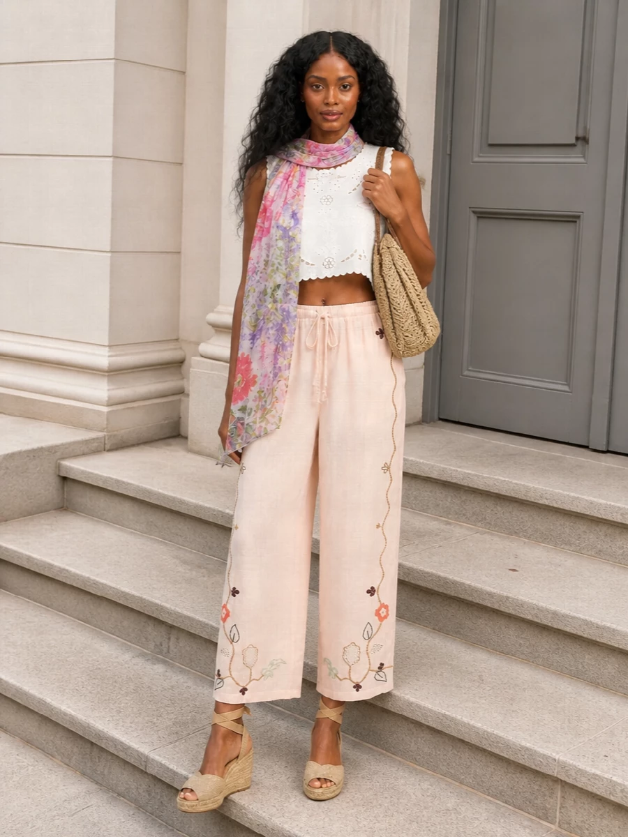 Soft blush embroidery meets airy white broderie in a cropped-on-cropped pairing that feels poetic but relaxed. Jute-wrapped wedges and a refined raffia tote bring warm, textural depth while still keeping the outfit light. The floral stole is a whisper of color you can drape or tuck away as the day unfolds.