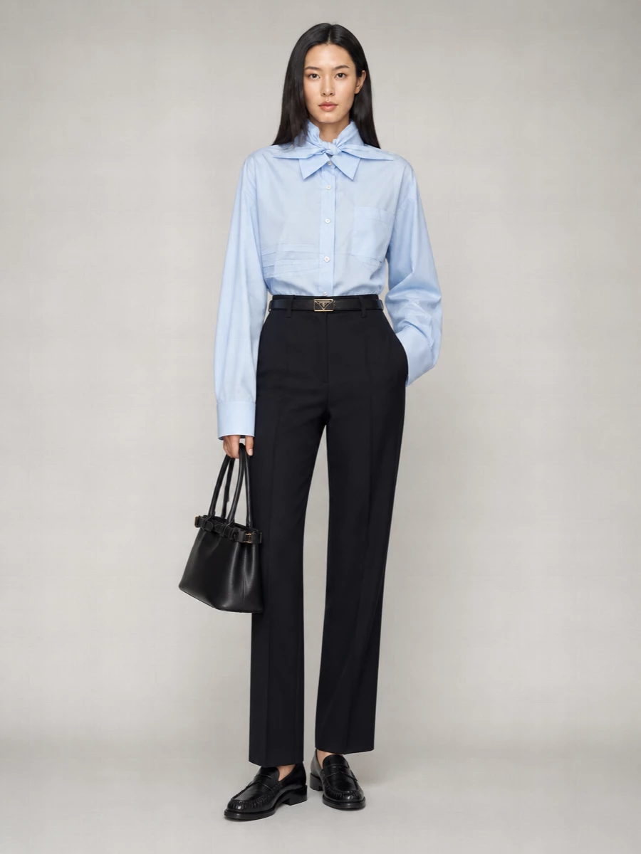 Pale blue poplin and deep navy wool form a clean, elongated column that feels precise without stiffness. A sharp black loafer and structured top-handle add Milanese rigor, while a slim logo belt quietly defines the high waist. The result is a controlled, modern uniform that moves easily from client meeting to late dinner.