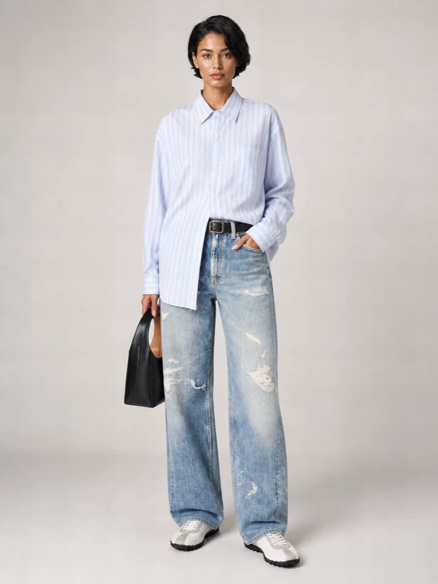 Our Legacy’s broken-in wide-leg denim is paired with an ice blue oversized striped shirt for a loose, borrowed ease that still feels considered. A slim black belt and structured black shoulder bag sharpen the midsection, while off-white Margiela sneakers keep the palette light and the mood urban and relaxed. It is an easy uniform for city days where you want slouch, length and just enough structure at the waist.