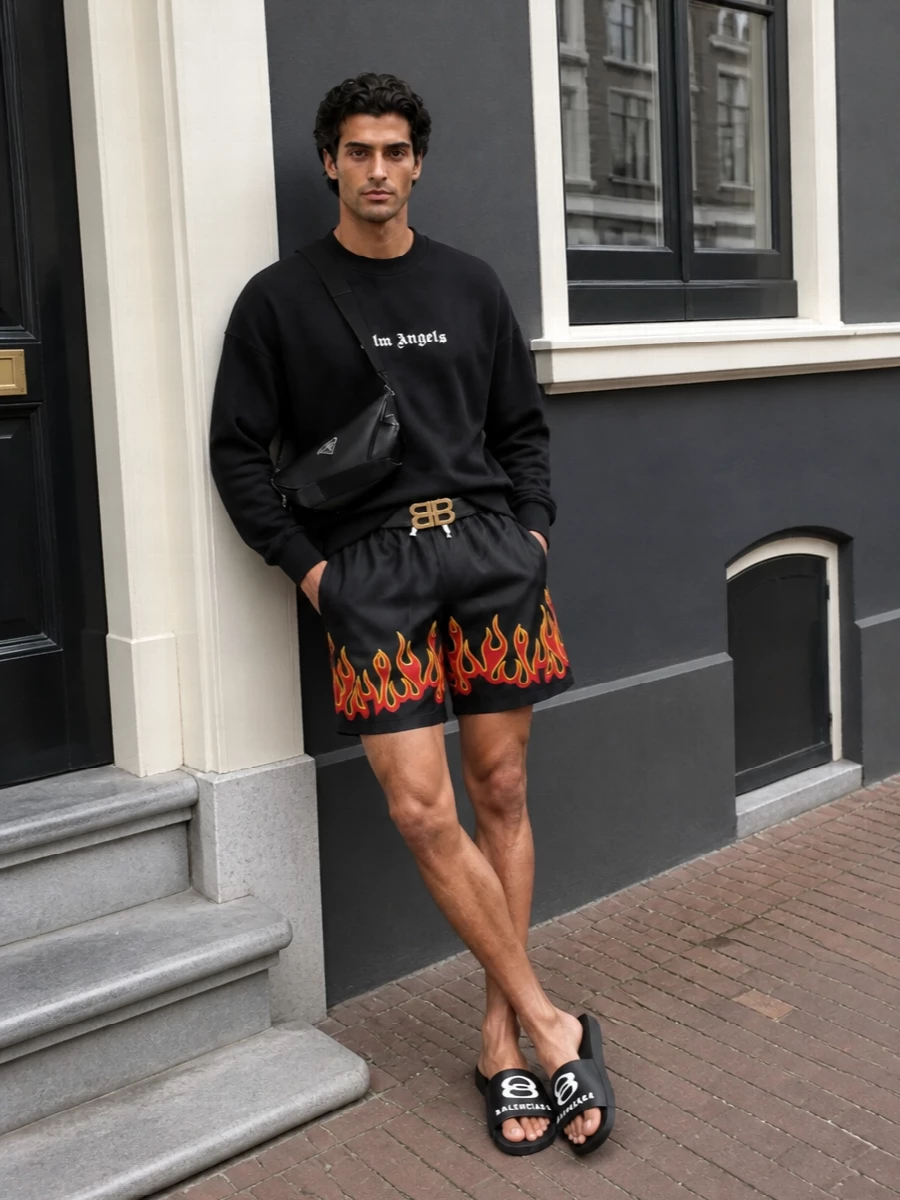 Flame-trimmed Palm Angels shorts meet a clean black logo crew for a tight, graphic street statement that still feels relaxed enough for poolside or city heat. Balenciaga slides keep the mood casual and directional, while a sleek Prada crossbody and a sharp logo belt bring just enough structure and designer polish to ground the attitude.