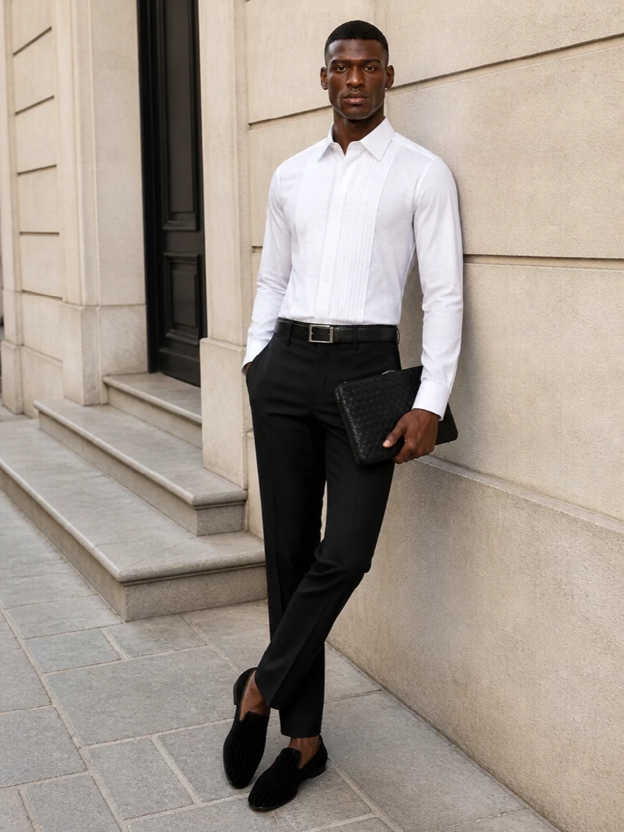This look is a disciplined, modern black-tie ensemble built around the Tom Ford pleated-front tuxedo shirt and sharply tailored black tux trousers. Velvet evening slippers keep the mood opulent yet understated, while a flat intrecciato clutch and minimal silver-buckled belt introduce just enough texture and shine to underline the quiet-luxury message without disturbing the clean, camera-ready silhouette.