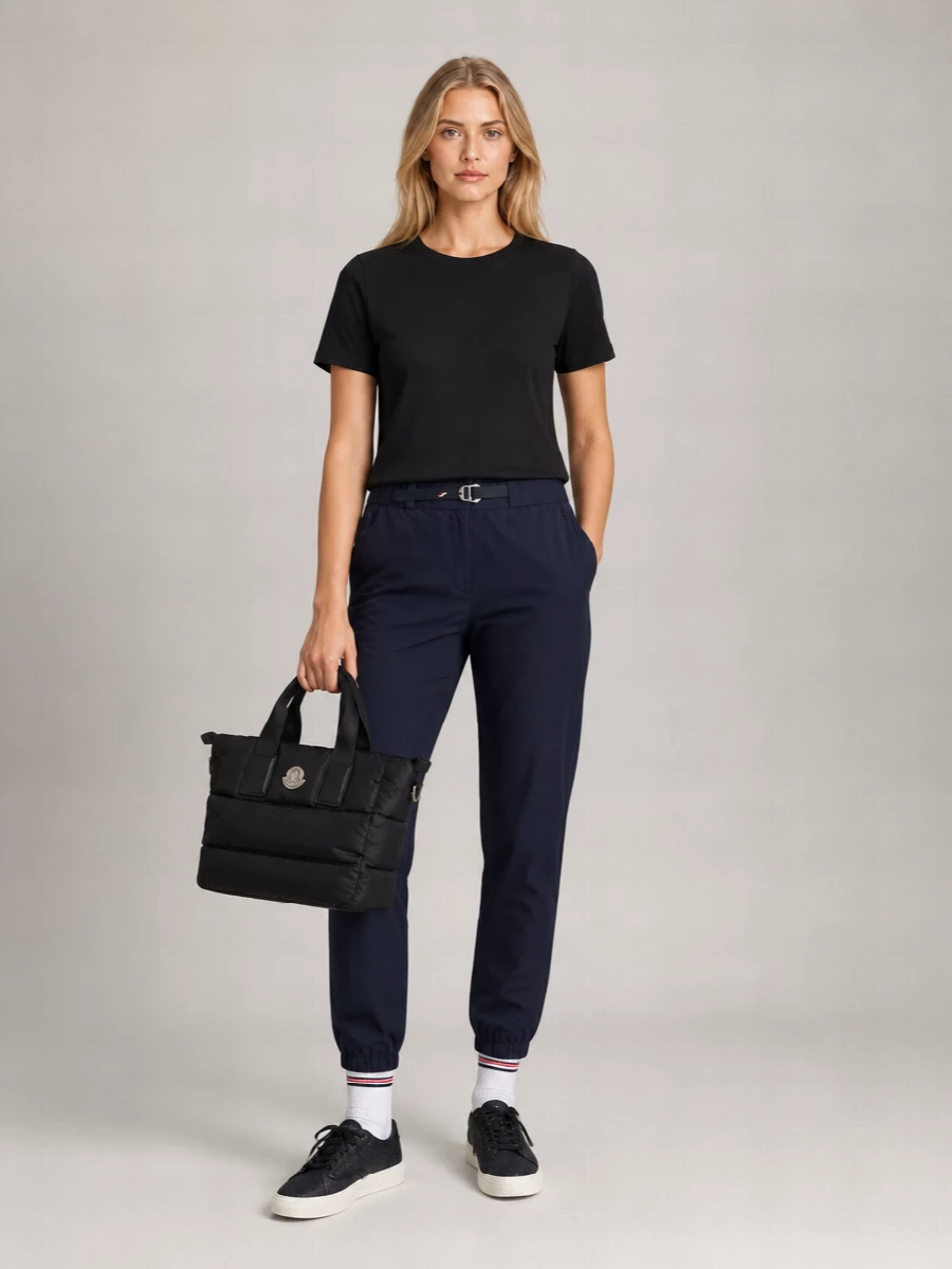 A monochrome Moncler tee meets a tapered navy jogger for a streamlined, sport-informed base that still feels considered in the city. Black leather sneakers and a padded tote hold the line at quietly polished, while soft white ribbed socks add a tiny hit of collegiate detail that keeps everything relaxed but intentional.