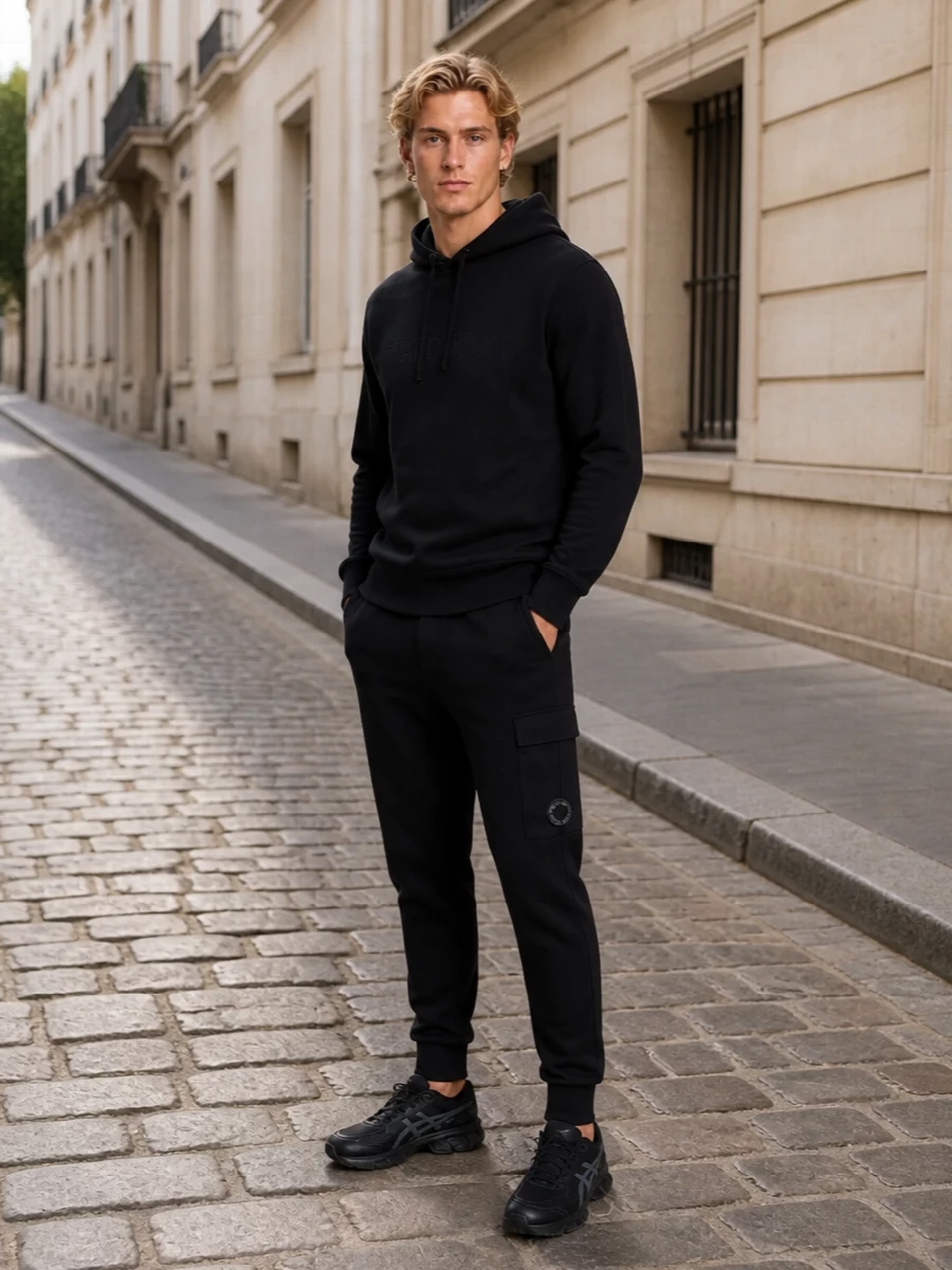 A fully monochrome, sport-driven combination that keeps the focus on clean lines and subtle tech detailing. The jogger, hoodie and runners align in a streamlined athletic silhouette, while the crossbody adds functional structure without breaking the black and charcoal story. It is built for movement, from winter commutes to long city days, with every piece reading quietly performance-led rather than logo loud.