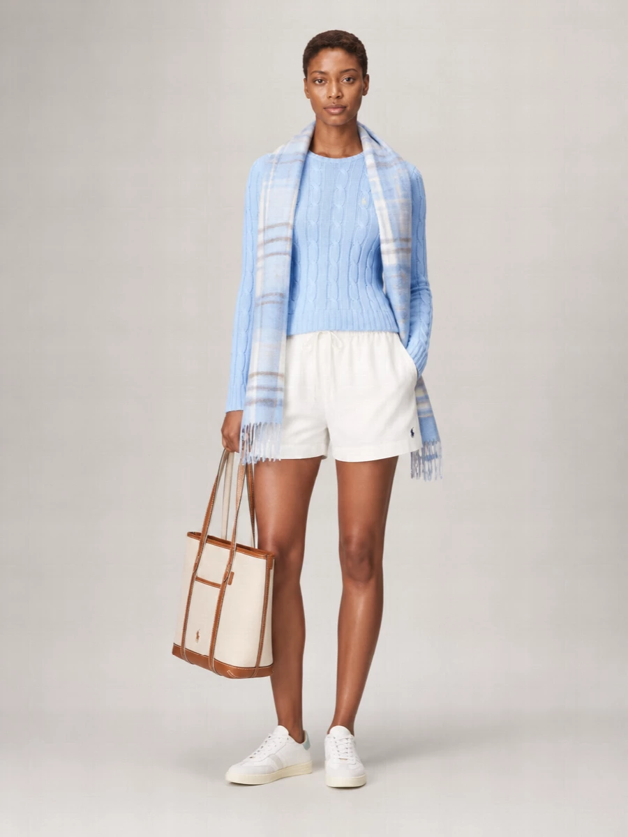 A sky blue cable knit meets airy off white shorts for a fresh, collegiate take on warm weather dressing. Soft white sneakers keep it relaxed yet considered, while the structured canvas tote adds a crisp heritage note. The powder blue scarf gently ties the palette together for cooler mornings and evenings.