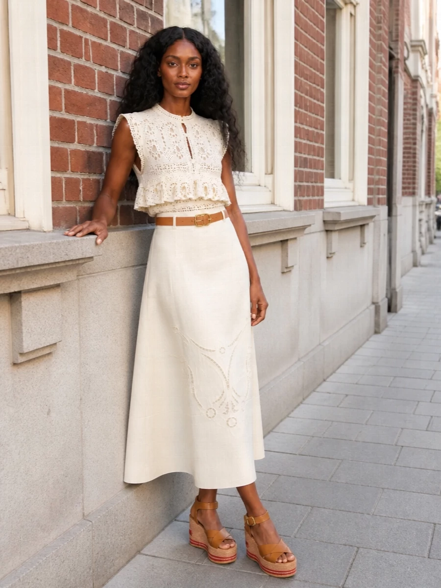 Romantic lace and tonal embroidery come together in a soft ivory-on-ivory pairing that feels light but considered, with the midi length keeping the ruffled crop refined rather than sweet. Tan leather accents and blush hardware warm the palette just enough, so the whole outfit reads as sunlit garden-party or terrace-dinner ready. Height at the shoe and a defined waist keep all that texture elongated and flattering rather than voluminous.