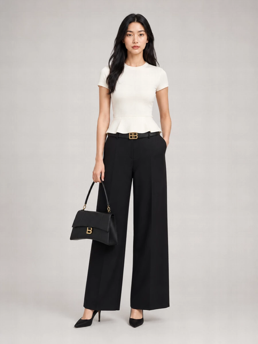 An ivory sculpted peplum top sharpens against high-waisted black wide-leg trousers, creating a long, precise line with a defined waist. Soft suede pointed heels and a structured black top-handle bag keep the palette tight and the finish quietly formal. A slim black belt punctuates the waist in gold, adding just enough focus without breaking the minimalist rhythm.