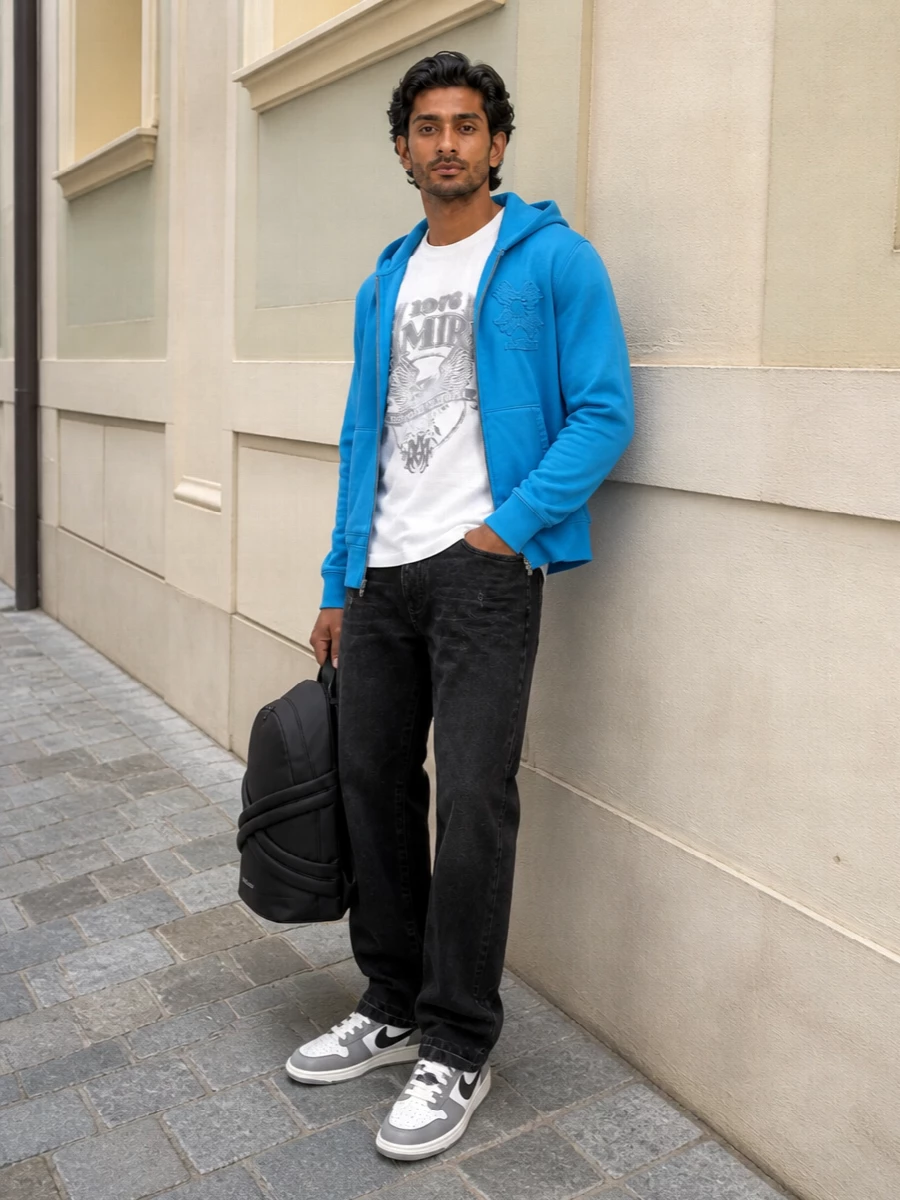Amiri’s azure hoodie sits over a white graphic tee and washed-black denim, giving a sharp LA street mix of saturation and monochrome. Paneled court sneakers and a sculptural black McQueen backpack keep everything grounded, graphic and ready for city days. The proportions stay relaxed and wearable, with the color hit focused up top so the outfit feels bold but not loud.
