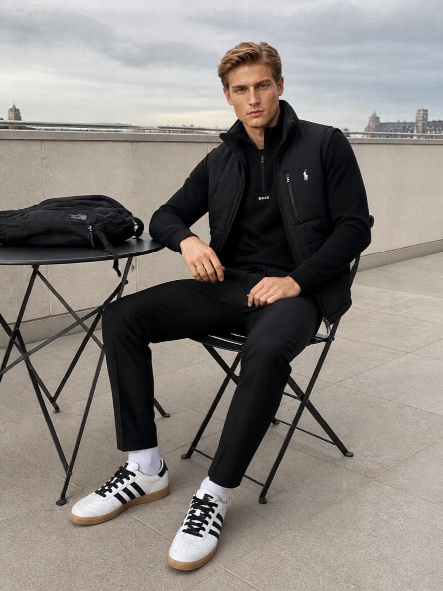 Ralph Lauren’s padded gilet anchors a monochrome, sport-preppy outfit built to move cleanly between commute, errands and casual office days. A black Boss half zip and Herno drawstring trousers keep the silhouette streamlined, while classic Adidas terrace sneakers and a technical North Face backpack underline the athletic, minimalist attitude without feeling overdesigned.