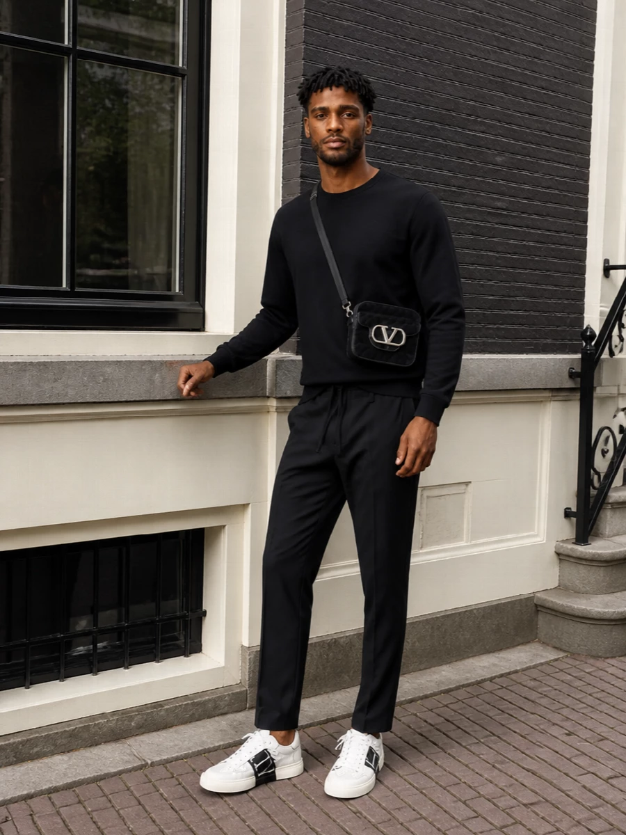 A pared-back black-on-black base lets the Valentino sneakers do the talking, framing their graphic band against a clean, streamlined silhouette. The tailored drawstring trouser keeps the line sharp while staying relaxed, and the textured crossbody quietly echoes the logo story without feeling loud. It is an easy uniform for city days where comfort and precision meet.