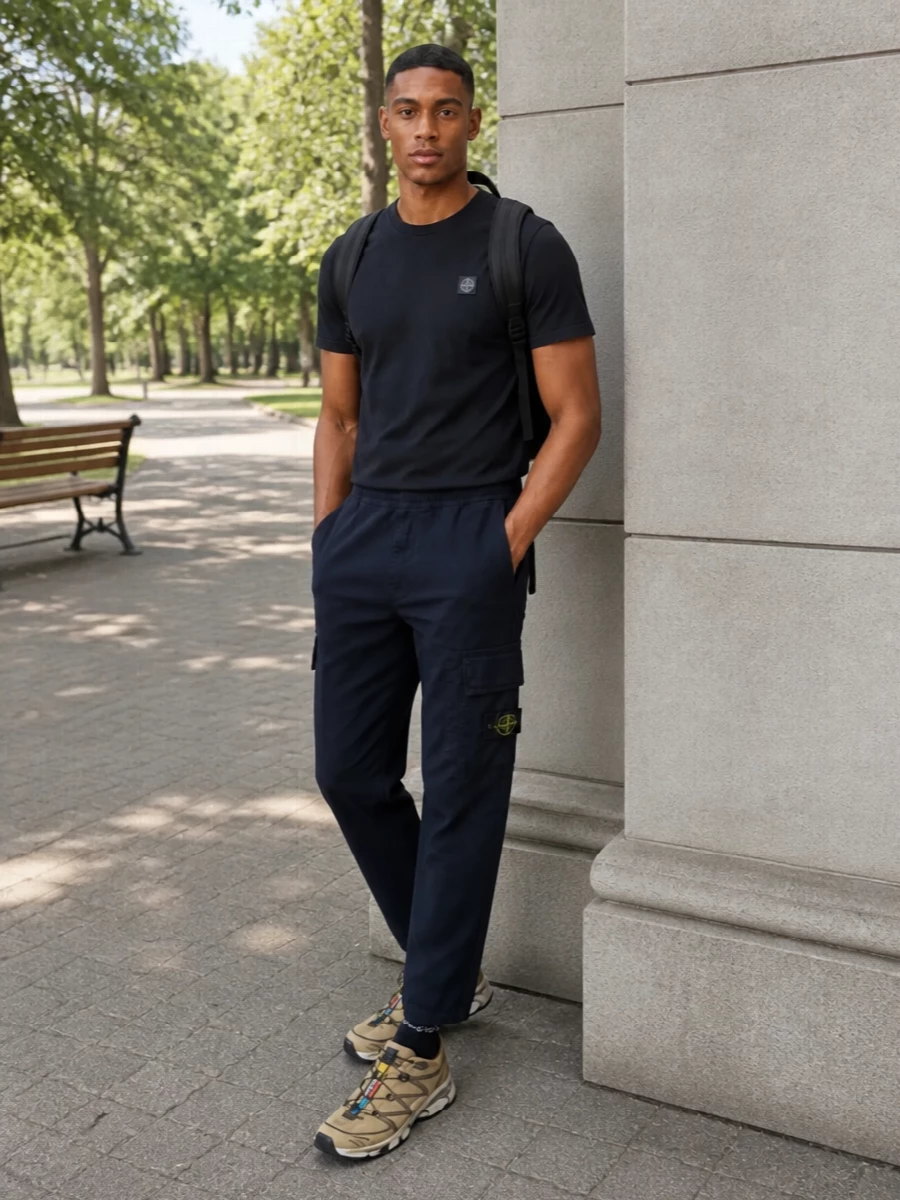 Navy Stone Island cargos and the matching compass tee create a tight, monochrome base that reads clean and technical. Sand-toned Salomon runners break the blue with a functional neutral hit, while the black Stone Island backpack and graphic socks keep the whole combination grounded in quiet, urban utility. It is an easy uniform for city days that still feels considered in its palette and proportions.