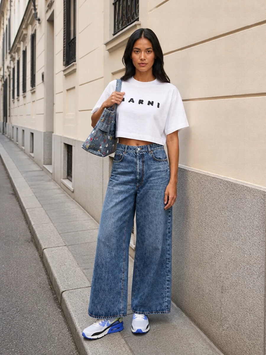 This is a clean, graphic take on double denim built around a cropped Marni logo tee and wide-leg Sportmax jeans that let the Marc Jacobs tote carry all the personality. The high rise and full volume of the jean balance the boxy crop on top, keeping proportions sharp while the sneakers lock in a city-ready, street-leaning mood. It is casual, design-led and easy to wear for all-day urban plans.