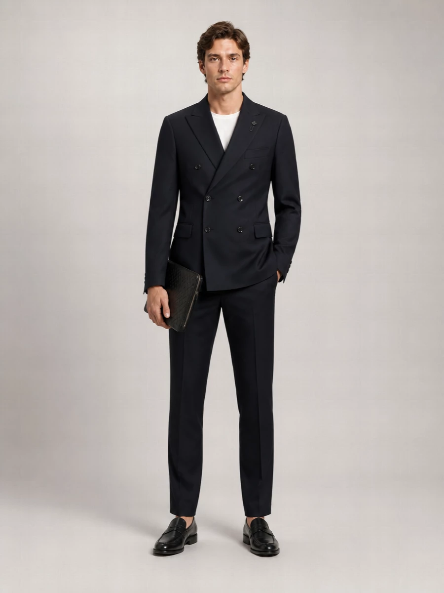Inky navy tailoring stays clean and modern here, with a double-breasted jacket sharpened by slim, creased trousers. Black penny loafers and a woven portfolio keep the mood quietly luxurious, ideal for business dinners that run late or polished city evenings. The palette stays deep and restrained so the interest comes from proportion, texture and cut rather than obvious branding.