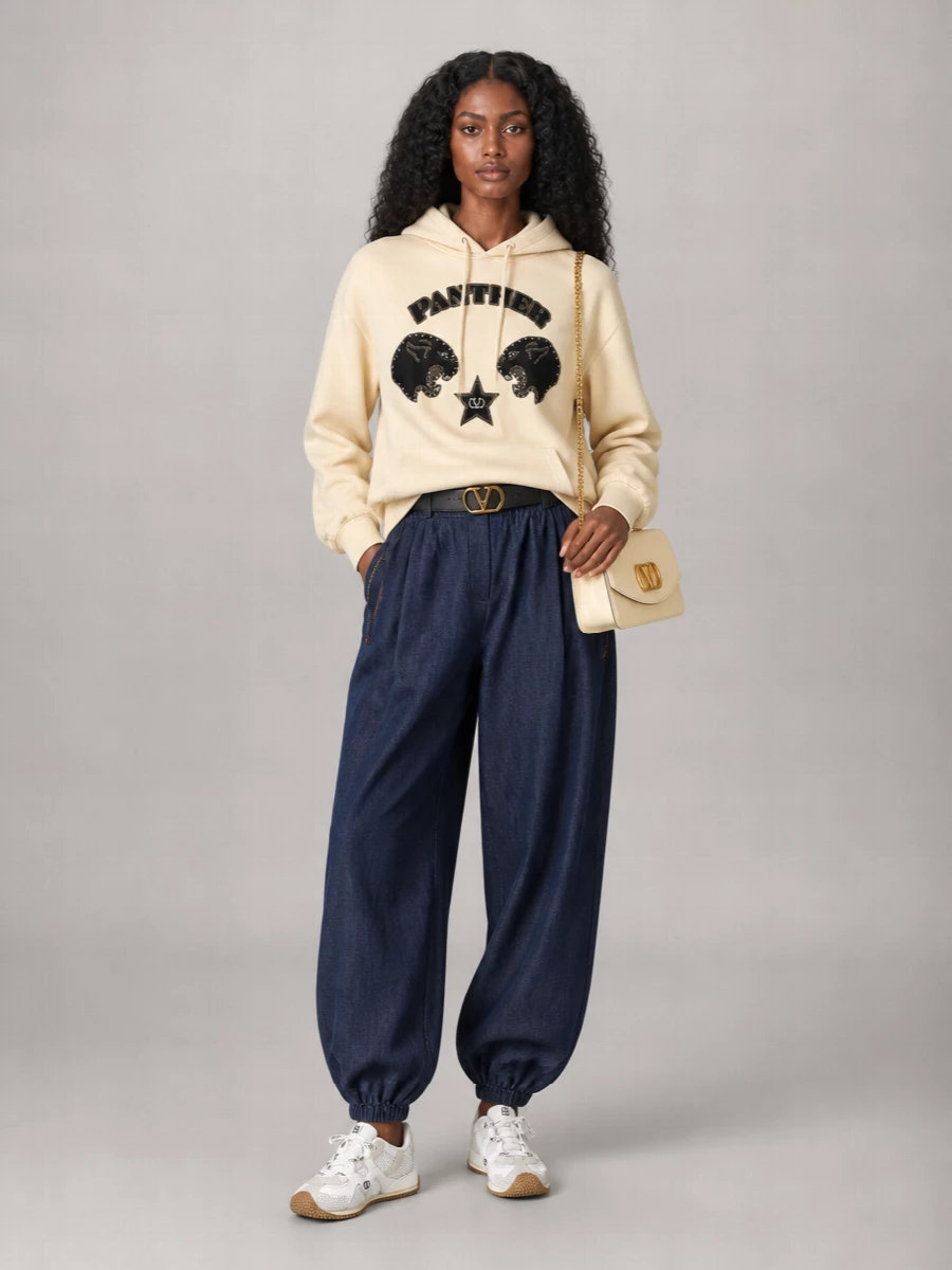 A buttercream graphic hoodie meets dark indigo joggers for a relaxed, sport-led silhouette that still feels sharply edited. Off-white technical sneakers keep the palette soft and grounded. A buttercream shoulder bag and discreet logo belt pull the neutrals together, giving the outfit a polished, streetwise finish.