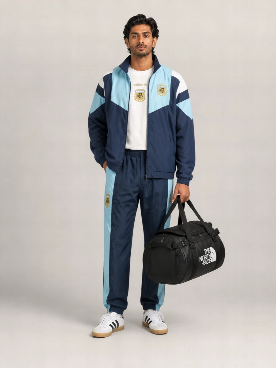 A fully dialed terrace-inspired Adidas outfit built around the AFA navy and sky blue track set, sharp enough for stadium seats and post-match streets. The matching tee and pants keep the color story tight, while white gum-sole sneakers and a black duffel anchor it in classic football-culture practicality. It is relaxed, uniform-like and clearly fan-coded without feeling like full replica kit cosplay.