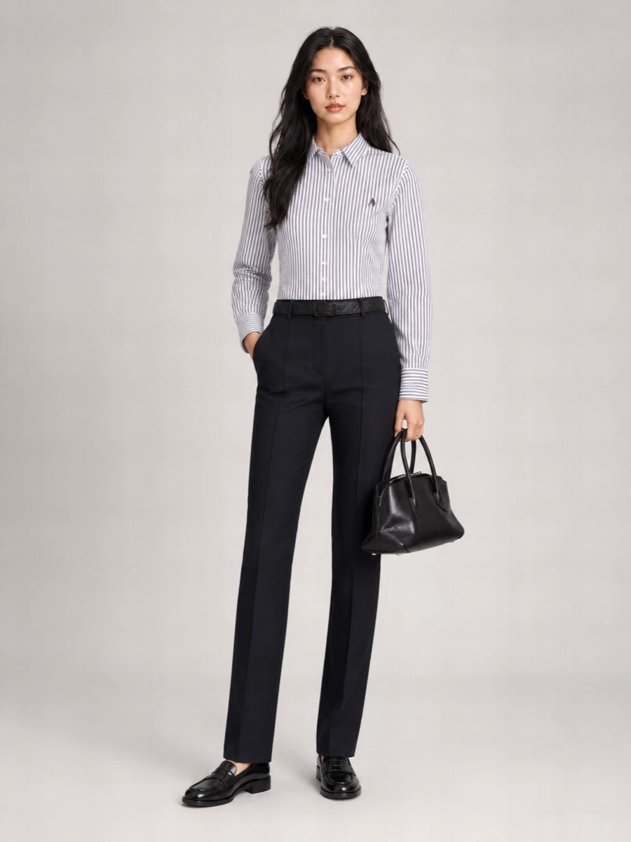 Crisp striped shirting meets elongated navy tailoring for a quietly assertive take on modern office polish. Glossy black loafers keep it grounded and androgynous, while a structured black top-handle and a slim black belt sharpen the finish without breaking the monochrome mood. It is a clean, confident uniform that reads considered from morning meetings to late dinners.