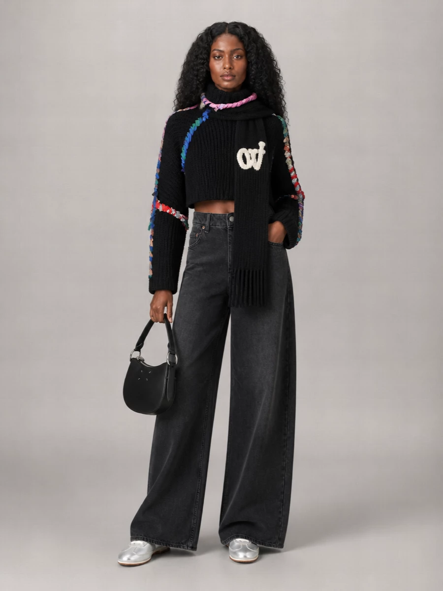 Marine Serre’s braided, cropped knit sits against high-rise washed black wide-leg denim, creating a clean architectural frame for all the color and texture up top. Metallic low-top sneakers keep the energy fast and sporty, while a curved Margiela shoulder bag and a graphic black-and-ivory scarf finish the palette in sharp, urban monochrome. The result is a streetwear set that feels graphic and sculptural but still easy to wear on repeat.