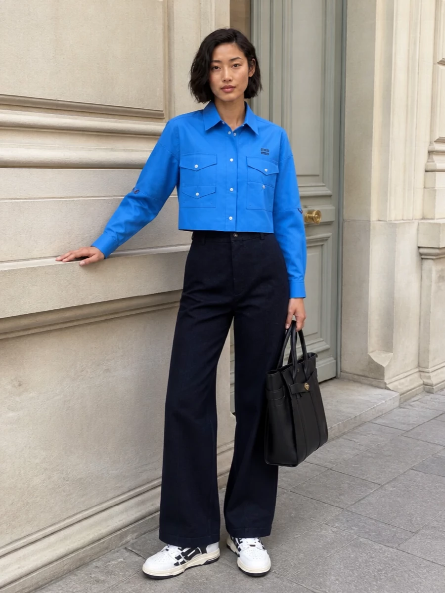 Crisp cobalt on top meets deep navy tailoring for a modern, preppy take on city dressing. The cropped shirt and high-rise wide-leg balance proportions, while monochrome sneakers and a structured navy tote keep the mood sharp and graphic. It is relaxed enough for daytime yet polished enough to carry into a casual dinner.