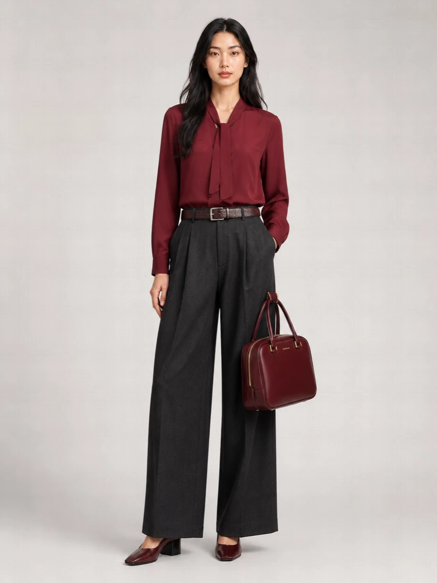 A deep burgundy tie-neck blouse sits against charcoal wide-leg tailoring for a quiet, boardroom-ready take on colour. Oxblood block-heel pumps and a structured bordeaux tote keep the line sharp yet warm for city days that drift into dinner.