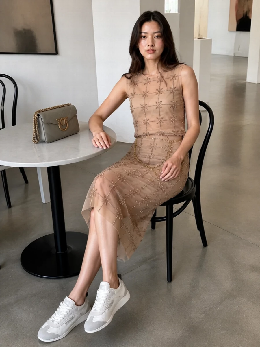 Head-to-toe beaded nude turns the tank into a statement twinset, with the matching Pinko pencil skirt elongating the line and catching light in one continuous shimmer. The soft dove-grey Love bag keeps hardware tonal while the fluid chain belt adds a deliberate hit of Y2K drama. Ground it with the clean knit sneakers for a modern, dressed-up yet relaxed take on summer nights out.