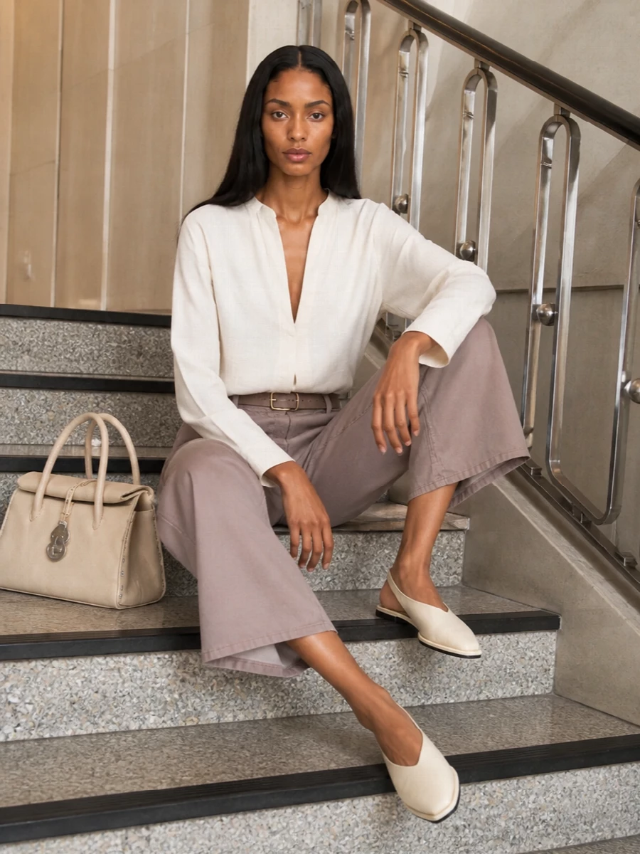 Soft neutrals do the work here, with taupe and ivory layered into a calm, tonal column that feels considered without reading formal. The fluid shirt and high-rise wide leg create an easy architectural line, lightly cinched with a slim belt so the proportions stay long and clean. Flat ivory slingbacks and a structured buttercream tote keep the finish modern and polished while still ready for real life.