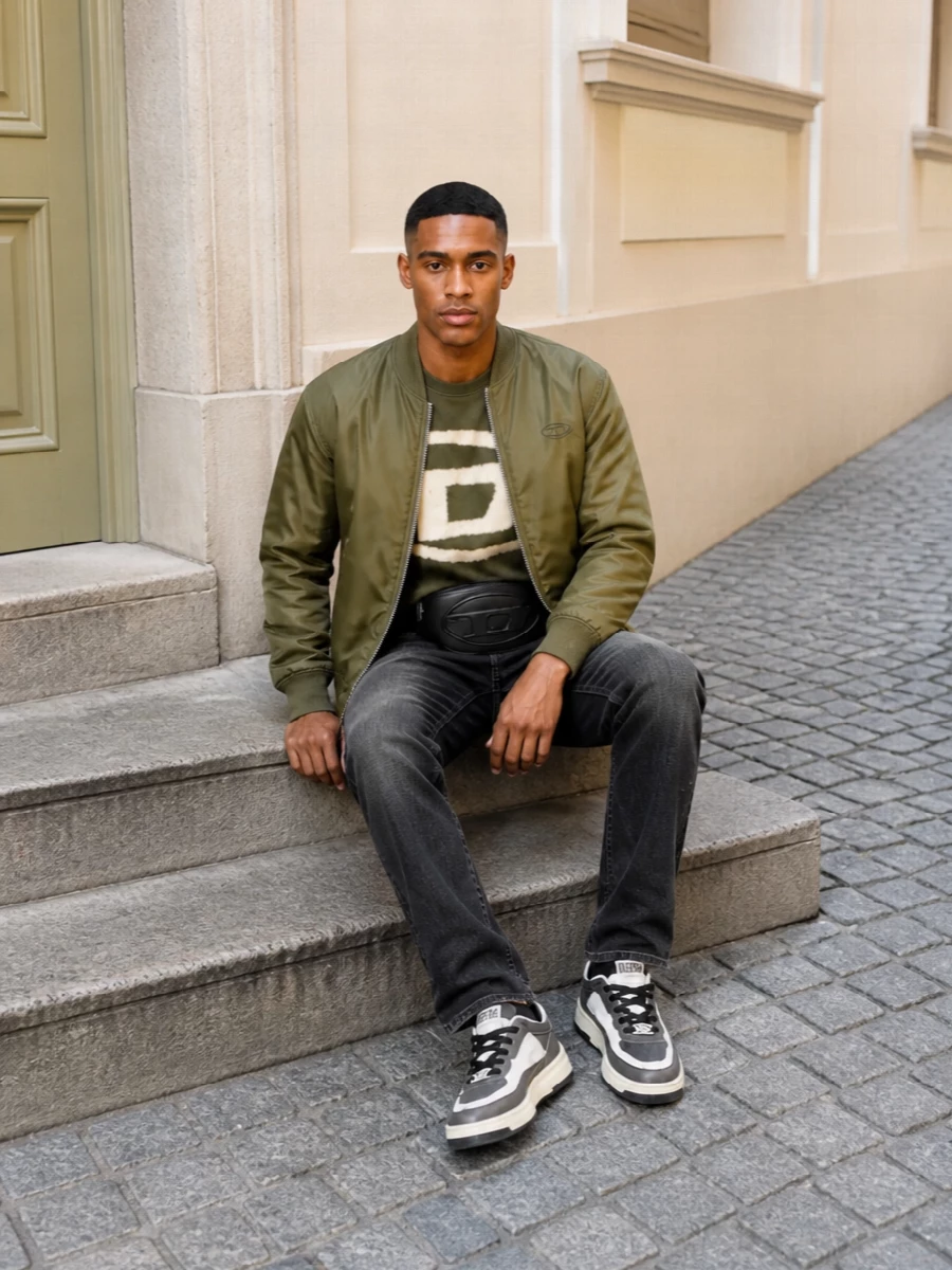 Olive and black do the heavy lifting here, giving the bomber a clear stage while the tie-dye logo tee injects that grungy Diesel hit. Straight black denim and charcoal sneakers keep the line easy and grounded, with a compact belt bag adding just enough utility to feel considered for city days. It is a confident, relaxed street uniform that leans into military tones without feeling costume-y.