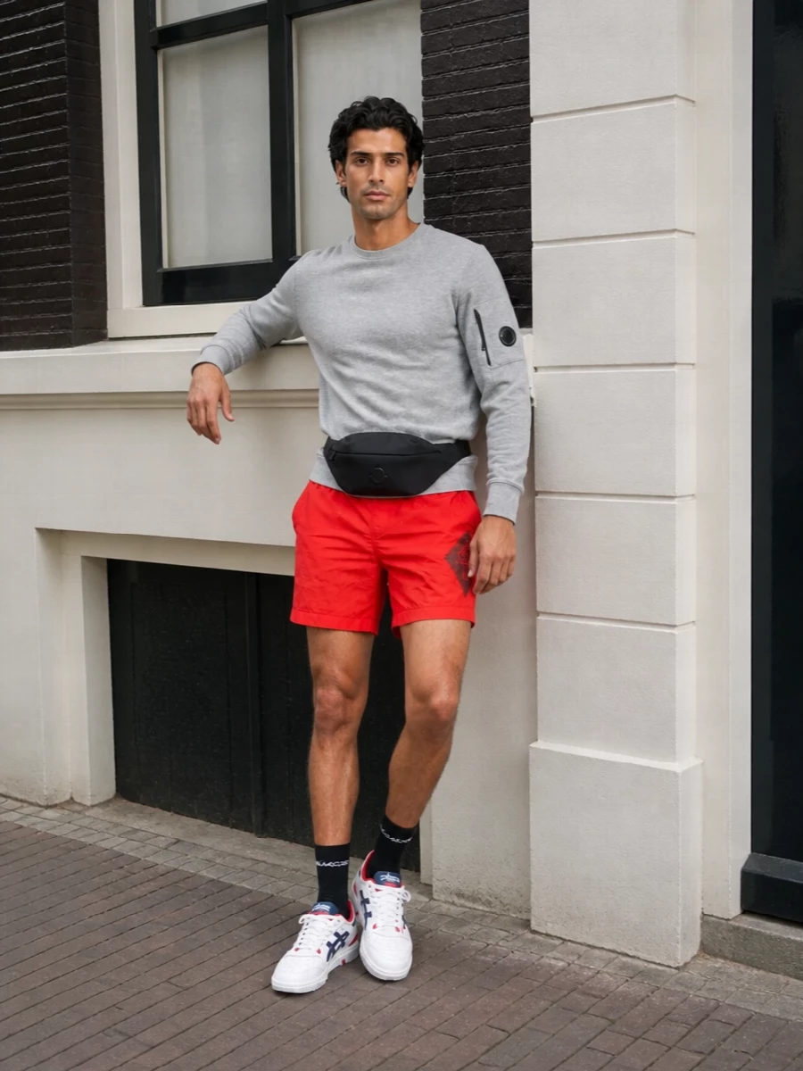 Neon red shorts stay front and center against the soft grey sweatshirt, giving you a clear, modern contrast that still feels relaxed and wearable. White court sneakers pick up the red and navy accents, keeping the energy athletic while the black belt bag and socks quietly ground everything. It is an easy city-to-beach combination that feels sport-driven but still polished enough for all-day movement.