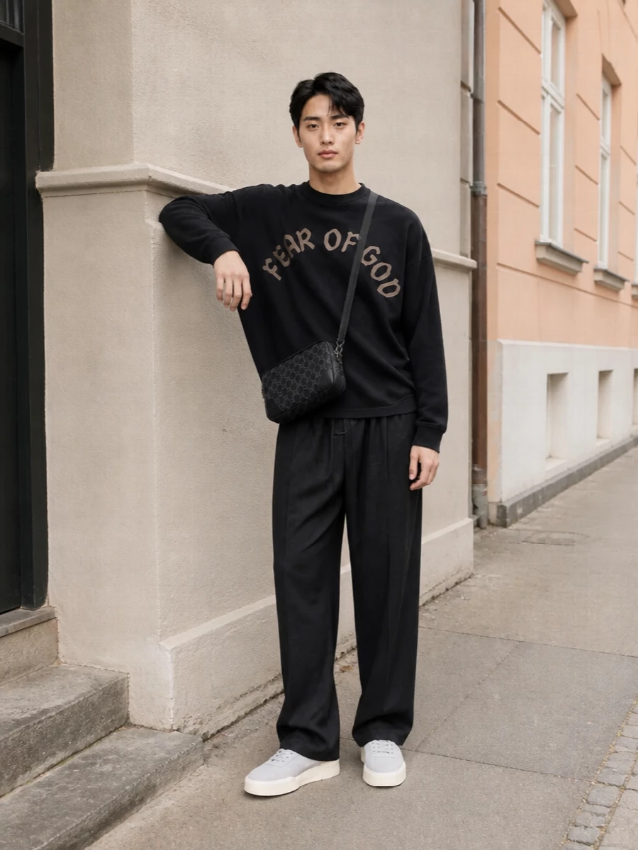 Washed black on charcoal creates a clean Fear Of God uniform, with the high‑rise wide leg echoing the tee’s slouch for a calm, elongated line. Soft grey sneakers and a compact dark crossbody break up the monochrome just enough, keeping the mood relaxed but precise for city days and low‑key nights.