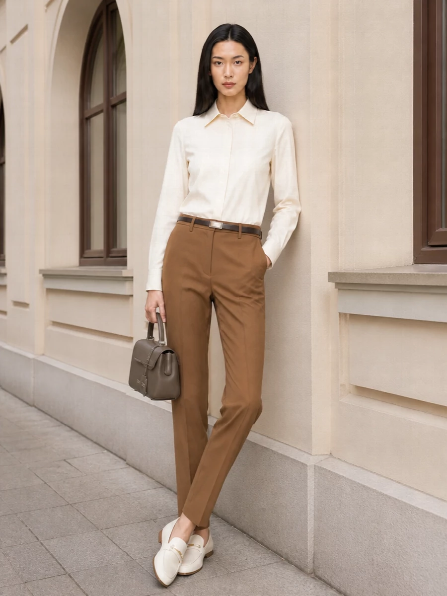 Camel tailoring is quietly softened by a buttercream shirt, creating a precise but gentle column of neutrals. Ivory loafers keep the mood light, while a structured taupe top-handle and slim belt refine the silhouette for serious days that still feel easy to wear. The result is modern boardroom polish with a calm, tonal warmth.