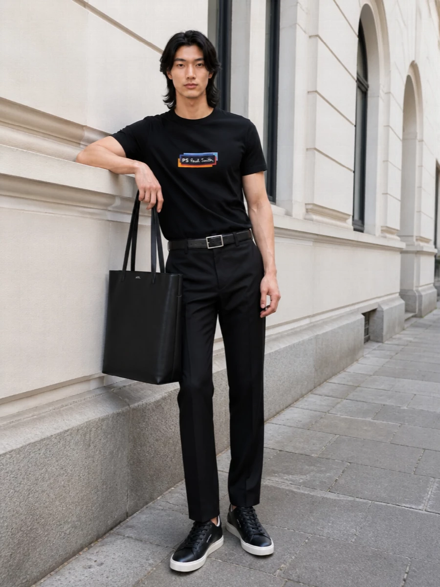 A black PS Paul Smith tee sits over equally clean black straight-leg trousers for a sharp, streetwear-preppy base that works from office casual to late city evenings. Black Paul Smith sneakers keep the line streamlined and graphic, while a structured A.P.C. leather tote and subtle striped Paul Smith belt bring just enough polish to feel considered without losing ease.