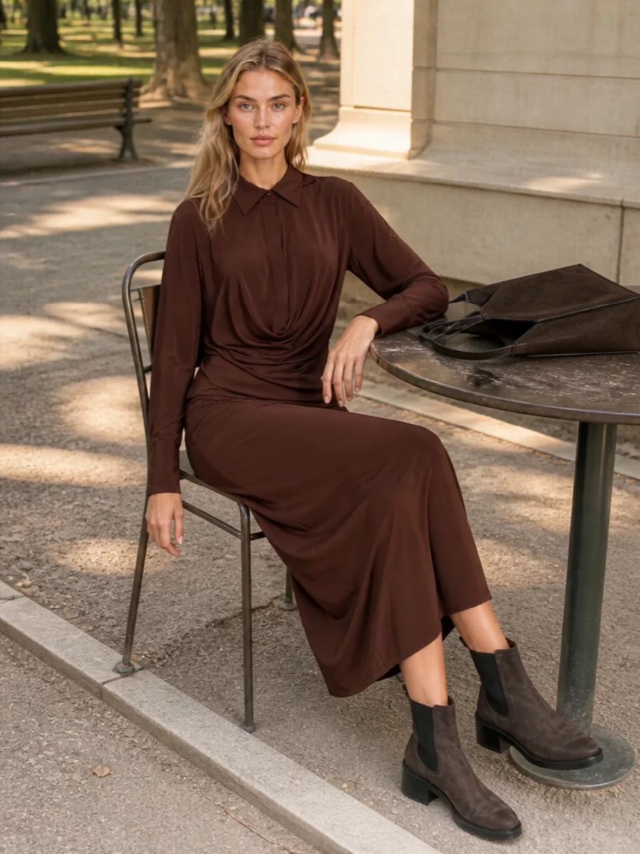 This is a head‑to‑toe chocolate story built around a single, draped midi dress, which best echoes the bag’s architectural lines and quiet, sculptural presence. The tailored cut and shirt collar keep it city‑ready rather than overtly evening, while the suede tote and block‑heel Chelsea boots add tactility and grounded height without breaking the tonal calm. It is an understated, richly brown ensemble that feels thoughtful for autumn days that can stretch into dinner.