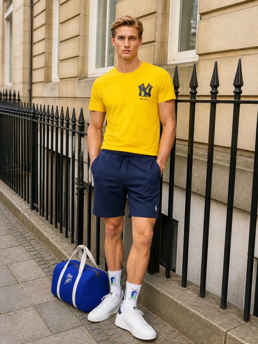 Bright collegiate yellow meets deep navy for a crisp, East Coast sport mood. The navy shorts and white court sneakers keep the graphic tee feeling grounded and easy, while the duffle and striped socks underline the relaxed, athletic attitude without adding fuss.