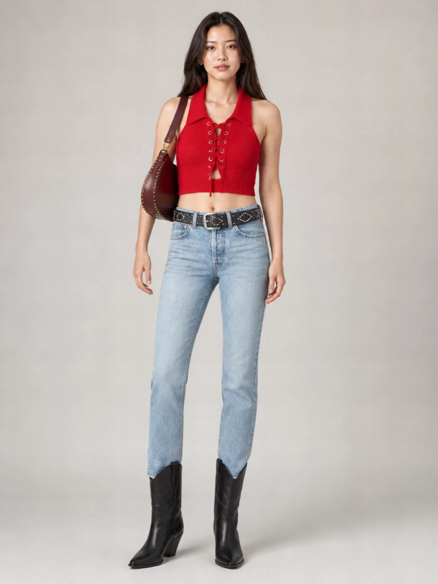A vivid red halter-knit meets light vintage denim for a mix of confidence and ease, all cut to keep the waist clean and legs long. Black western boots and a studded belt add just enough rock tension, while a burgundy crescent bag deepens the palette without fighting the red. It is relaxed streetwear with a polished boho edge, ready for city days that run late.