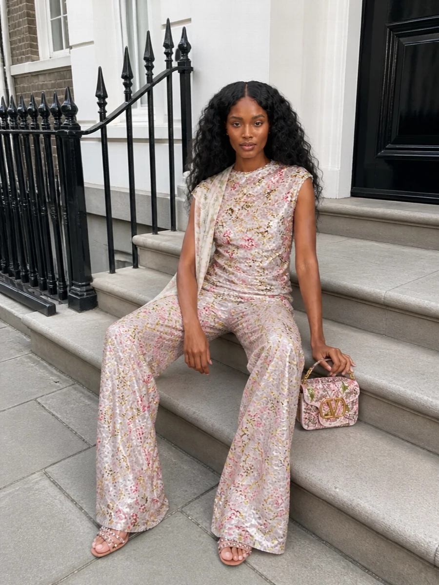 A head-to-toe Alberta Ferretti sequinned set turns the floral wide-leg trousers into a full, shimmering column, keeping the mood romantic and softly Y2K while feeling refined enough for cocktails or weddings. Rose-gold crystal sandals peek out from the pooling hem, and a floral Valentino mini bag subtly repeats the garden palette so the whole ensemble reads cohesive rather than busy. A gauzy printed stole is there for a whisper of coverage and movement, not to interrupt the liquid shine.