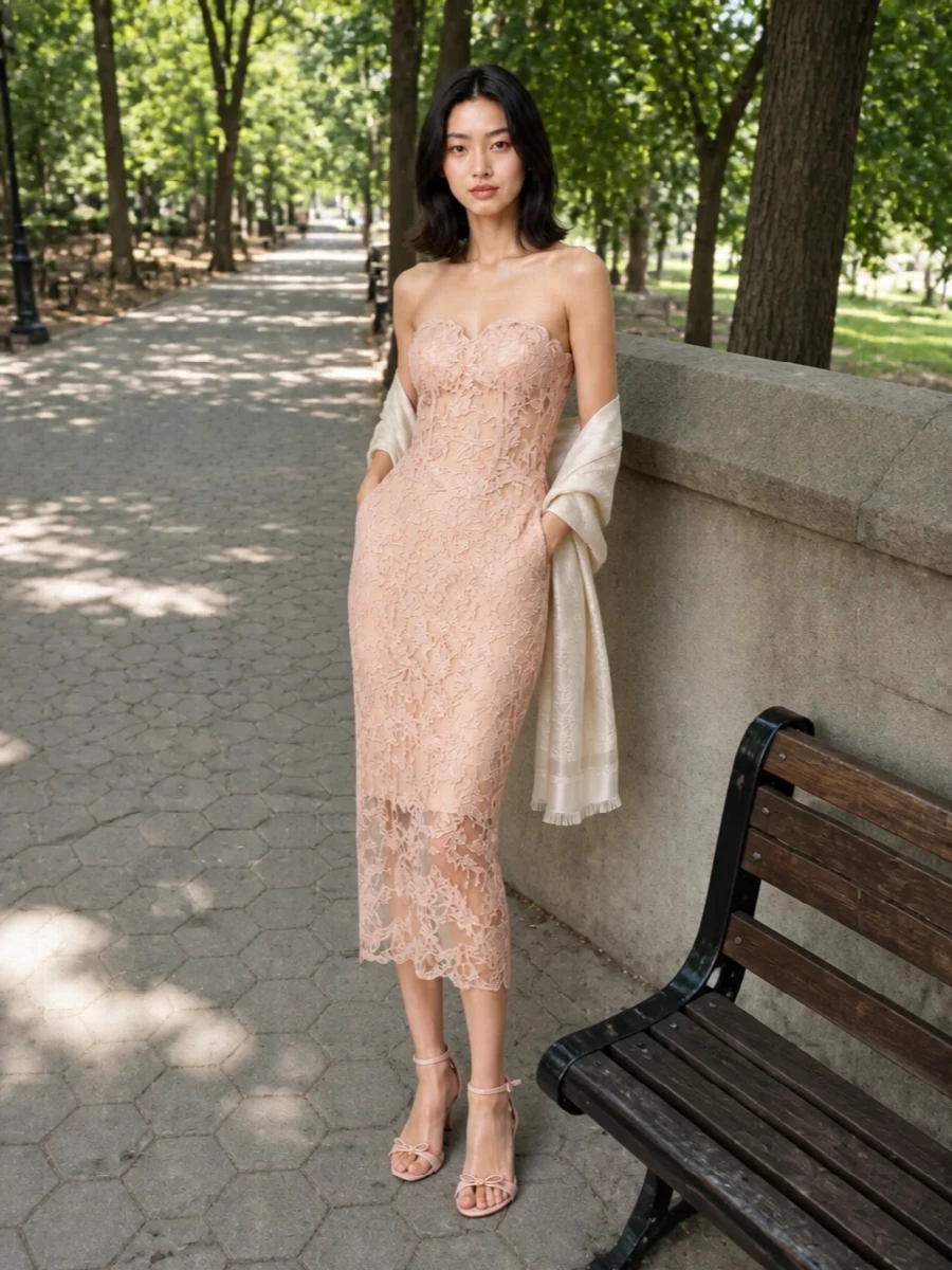 A blush lace column like this deserves accessories that whisper, not shout. Nude-blush straps and a powdered-satin clutch keep the focus on the corseted silhouette, while a gauzy neutral stole adds just enough softness over bare shoulders. The result is a quietly luminous cocktail ensemble that feels intimate, romantic and impeccably composed for warm summer evenings.