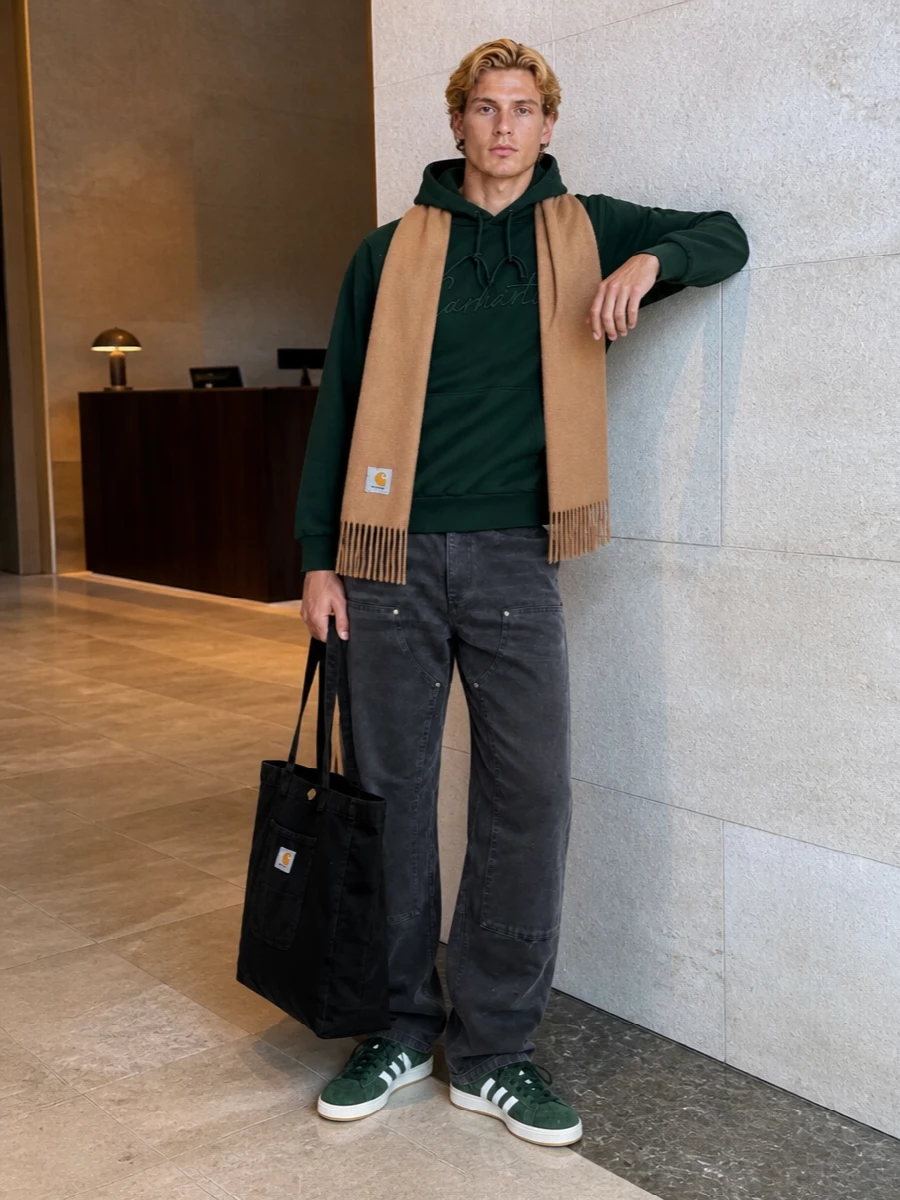 Deep forest Carhartt fleece meets washed charcoal work pants for a relaxed, skate-adjacent uniform that still feels put together. Forest green suede sneakers echo the hoodie tone, while the oversized black tote and camel scarf keep the palette grounded, practical and city-ready.