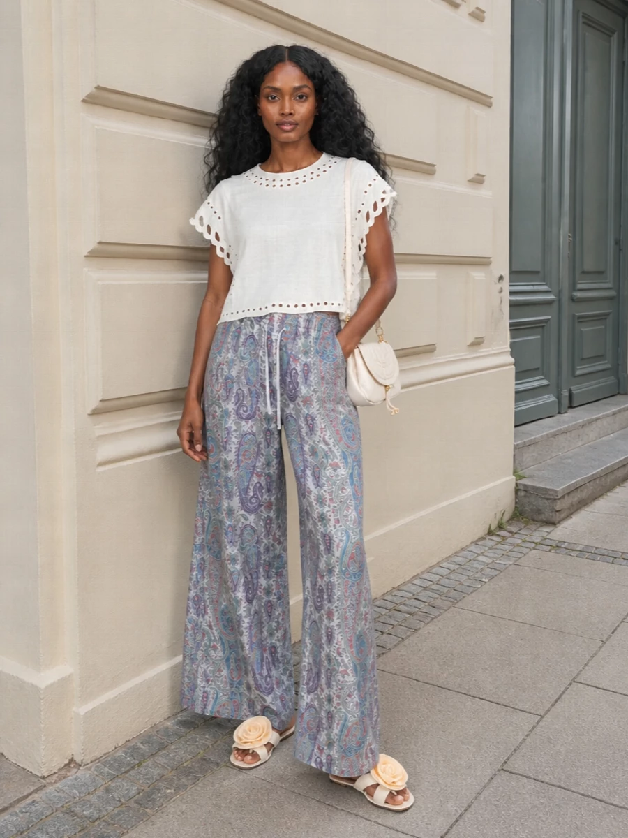 An airy ivory eyelet blouse meets fluid Etro paisley trousers for a soft, boho-romantic mix of texture and pattern in pale, sun-faded tones. Flat floral sandals keep the mood relaxed and feminine, while a small ivory Chloé shoulder bag adds just enough polish for city afternoons or holiday dinners.
