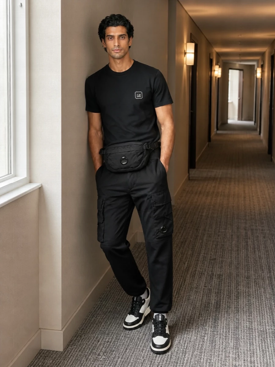 Monochrome C.P. Company pieces keep the energy low-key and technical, with the straight black cargos grounding the clean logo tee. Graphic black and off-white sneakers and a compact belt bag sharpen the streetwear edge while staying practical. A subtle hit of striped sock shows you have thought about the details without overworking them.