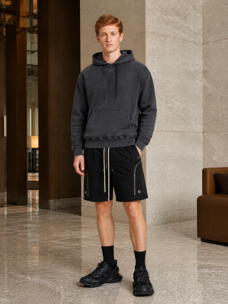Relaxed Rick Owens shorts ground a monochrome, utility-led streetwear story, with the washed charcoal hoodie softening the industrial hardware and drawcords. All-black Balenciaga runners and a matching crossbody keep the energy technical and urban while staying practical enough for long city days. The result is graphic but controlled, built around comfort, function and a quietly aggressive silhouette.